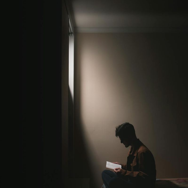 Person meditatively sitting in a dark minimalist room.