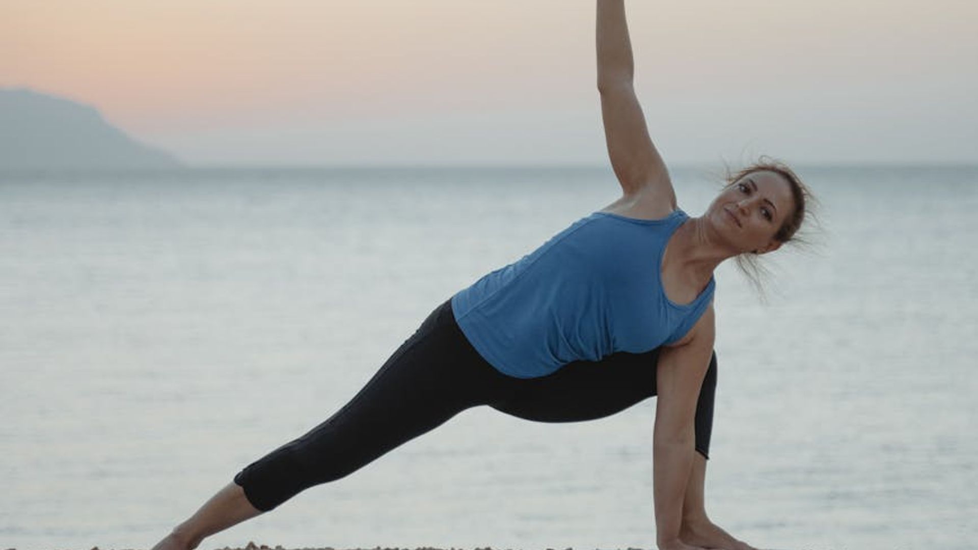 Serene person practicing yoga at dawn near a calm lake.